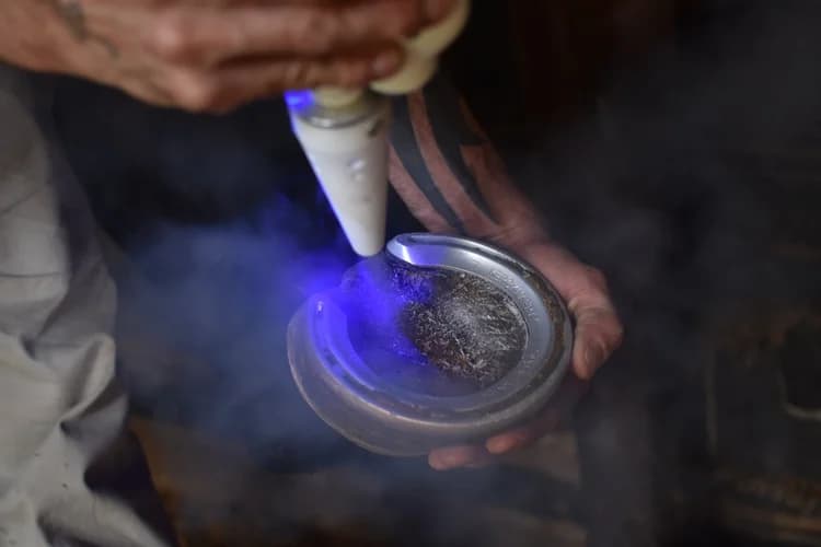 Farrier applying a blue light tool to a horse's hoof and horseshoe with smoke.